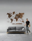 Man standing next to a gray sofa with a XL size world map wall decoration on a gray wall.