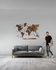 Man standing next to a gray sofa with a large size wooden world map wall decoration on a light gray wall.