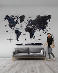 Man standing next to a large world map wall decal in a room with a gray sofa.