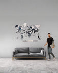Man standing next to a gray sofa with a medium size wooden world map wall art on a gray wall.