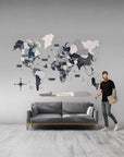 Man standing next to a world map wall art in a room with a gray sofa.