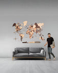 Man standing next to a XL size world map wall decoration in a room with a gray sofa.