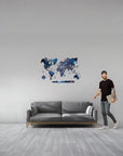Man standing next to a gray sofa with a world map wall decal in a room.