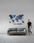 Man standing next to a gray sofa with a world map wall decal on a gray wall.