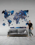 Man standing next to a gray sofa with a world map wall decal in a room.