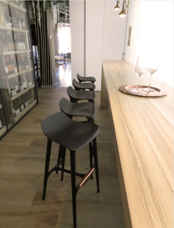 European luxury bar stools, like the Agrippa Morgan Bar Stool or Agrippa Spain, line a sleek black row in a luxurious bar.