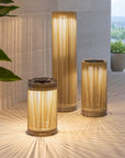 Three cylindrical outdoor lamps on a wooden floor with a blurred natural background by Les Jardins available at Spacio retail stores in India.