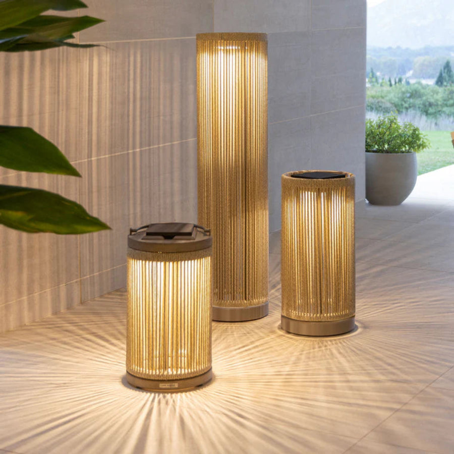 Three cylindrical outdoor lamps on a wooden floor with a blurred natural background by Les Jardins available at Spacio retail stores in India.