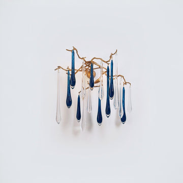 A wall light with glass droplets in clear and blue colour hanging from gold finish branches on a light grey colour backgroud