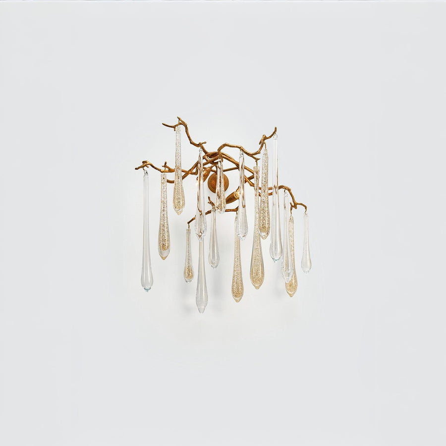 A wall light with glass droplets in clear and gold colour hanging from gold finish branches on a light grey colour background