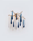 A wall light with glass droplets in clear and blue colour hanging from gold finish branches on a light grey colour backgroud