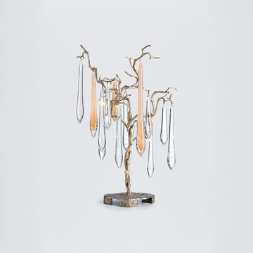 A table lamps with water droplet shaped glass hanging from gold colour branches on a light grey colour background. 