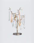 A table lamps with water droplet shaped glass hanging from gold colour branches on a light grey colour background. 