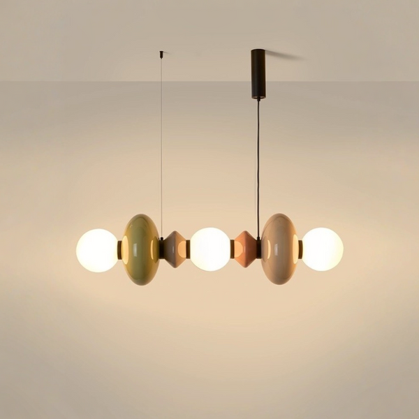 A modern multi-light linear pendant chandelier with glossy, rounded bulb-shaped shades in muted olive green, cream, and terracotta, suspended by black cords against a warm beige wall.