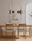 A modern dining room scene featuring a light wood dining table and six matching chairs with beige upholstered seats, under a multi-colored geometric pendant light.