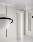 A round wall light next to a long wall mirror in a corner of a an empty room. 