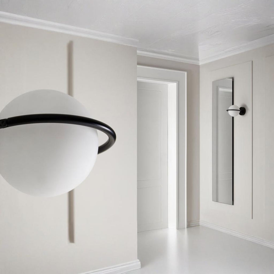 A round wall light next to a long wall mirror in a corner of a an empty room. 