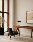 A study corner in a large double height room with a chair, planter, wall art and a table lamp. 