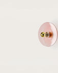 A pink colour wall light in shape of a disc on a light cream colour background