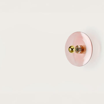 A pink colour wall light in shape of a disc on a light cream colour background