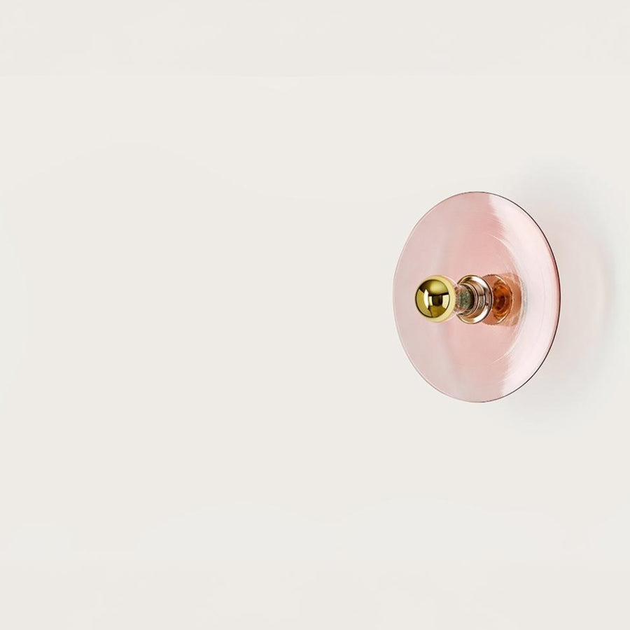 A pink colour wall light in shape of a disc on a light cream colour background