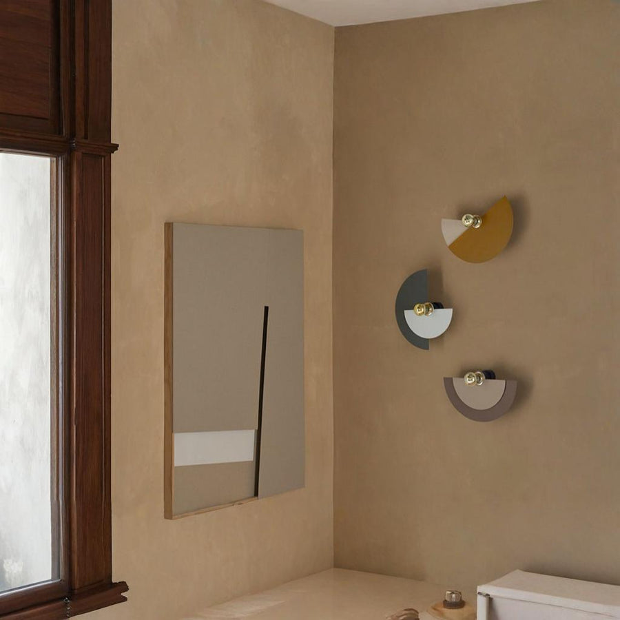 4 Wall lights in different colours discs in different colours in the corner of a room on a beige colour wall. 