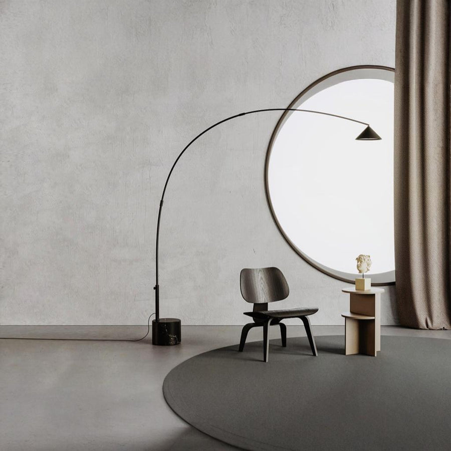 A modern design floor lamp in marble and metal in front of a large round window and chair in a grey beige theme room. 