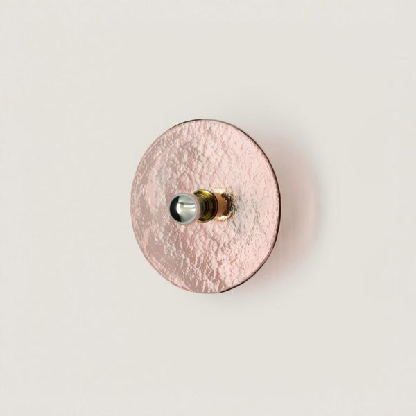 A pink colour textured glass wall light in shape of a disc on a light cream colour background