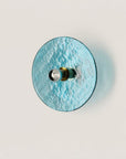 A blue colour textured glass wall light in shape of a disc on a light cream colour background