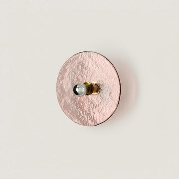 A pink colour textured glass wall light in shape of a disc on a light cream colour background