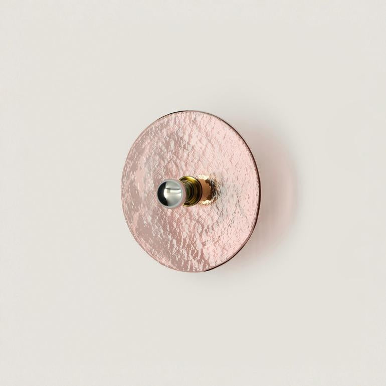 A pink colour textured glass wall light in shape of a disc on a light cream colour background