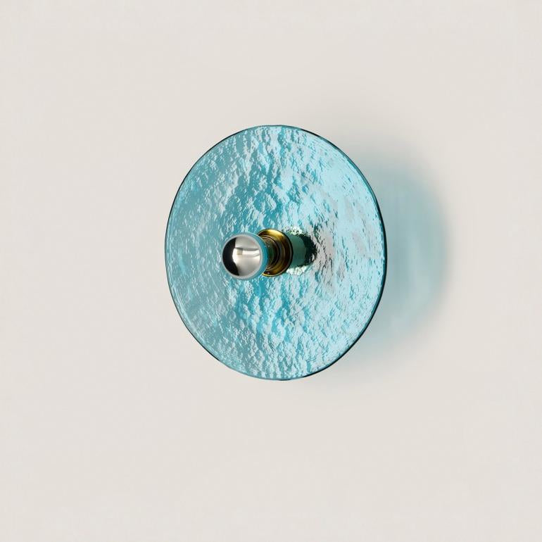 A blue colour textured glass wall light in shape of a disc on a light cream colour background