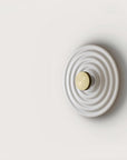 A round disc wall light on a light grey back ground. 