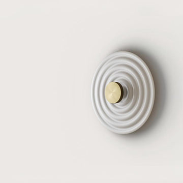 A round disc wall light on a light grey back ground. 