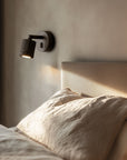 A modern wall bedside lamp next to a beige colour bed