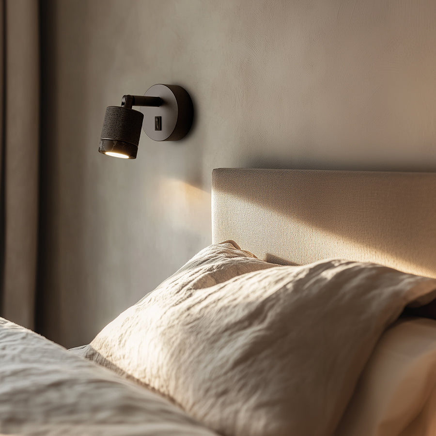 A modern wall bedside lamp next to a beige colour bed