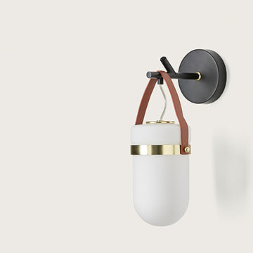 A wall light in the shape of a lantern hanging from a black metal branch on a light cream colour background