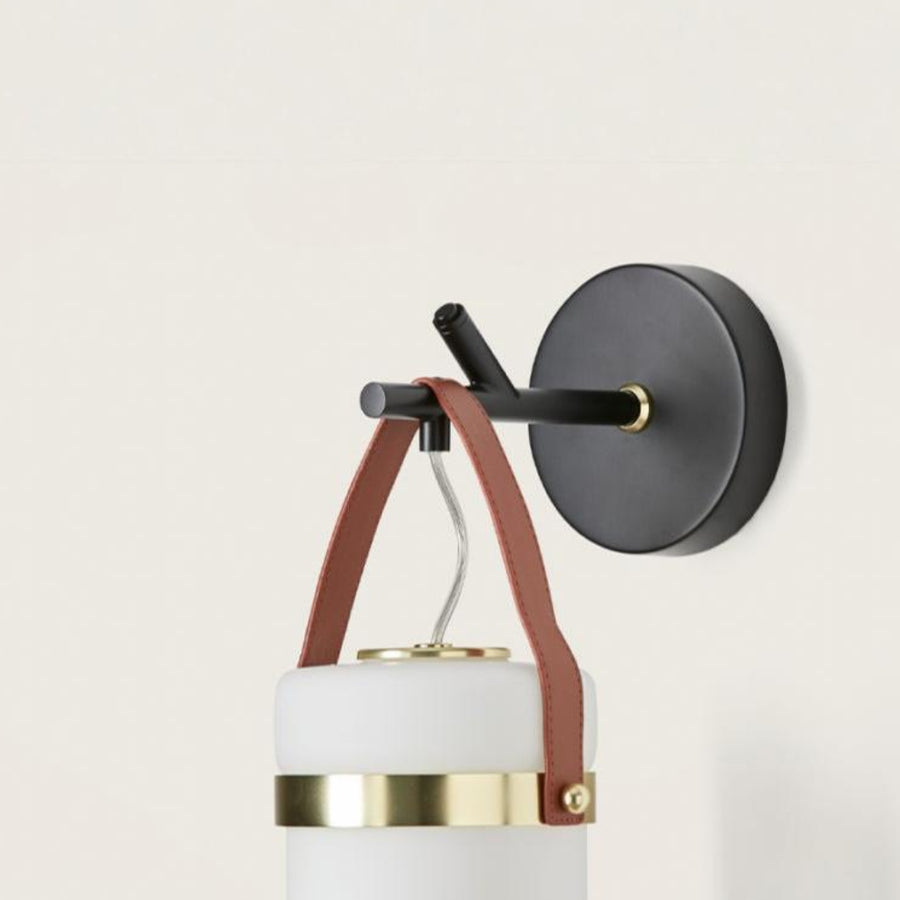 Close up of wall light in the shape of a lantern hanging from a black metal branch on a light cream colour background from the Almon collection of Aroma Del Campo, available at Spacio in India. 