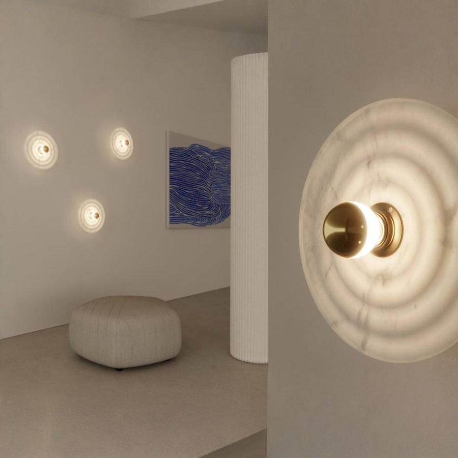 A living space with an ottoman, blue colour painting and 4 wall lights made of alabaster marble. 