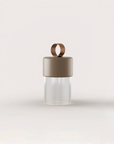 A minimalist portable and rechargeable table lamp with a matte taupe-brown cap, a matching carrying loop, and a ribbed clear glass crystal lower body, centered on a light off-white background.
