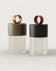 Two modern cylindrical portable and rechargeable with ribbed clear lower bodies, matte olive green and black upper sections, and circular copper-toned ring handles, photographed on a clean light beige background.