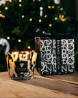 Baobab Black Pearls Candle Max 10 glowing beside gift box with festive lights and Christmas tree in the background, perfect for gifting from Spacio India.