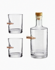 Clear glass decanter and two glasses with bullet-shaped copper stoppers on a white background