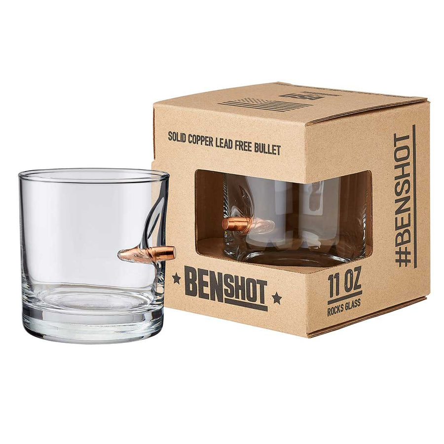 Clear glass shot glass with bullet design next to its packaging box on a white background