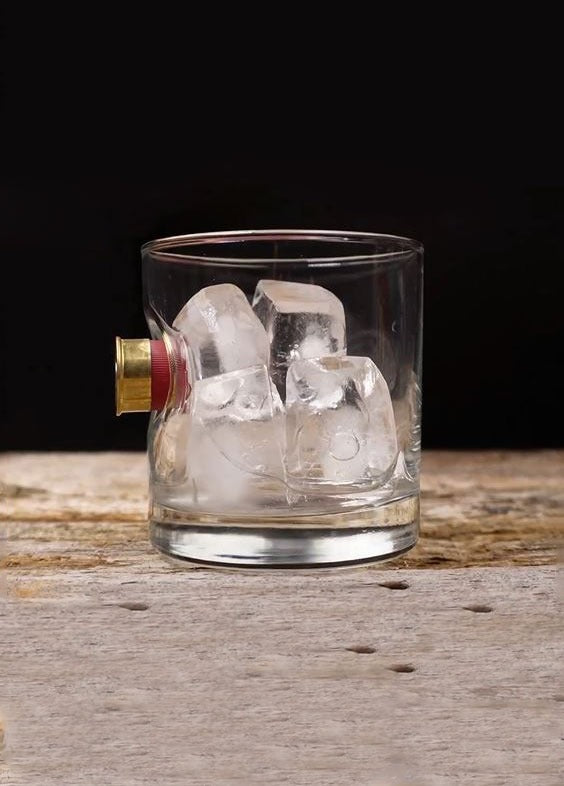 Clear glass with ice cubes and a bullet casing on a wooden surface