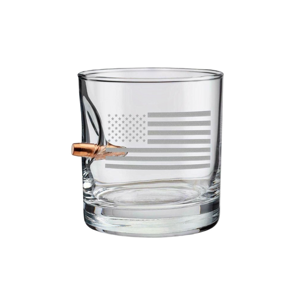 Clear whiskey glass with American flag engraving and a bullet casing on a white background from the American brand Benshot available at Spacio retail stores in Mumbai & Kolkata. 