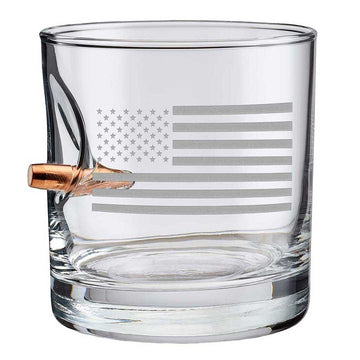 Clear whiskey glass with American flag engraving and a bullet casing on a white background from the American brand Benshot available at Spacio retail stores in Mumbai & Kolkata. 