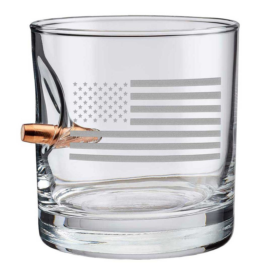 Clear whiskey glass with American flag engraving and a bullet casing on a white background from the American brand Benshot available at Spacio retail stores in Mumbai & Kolkata. 