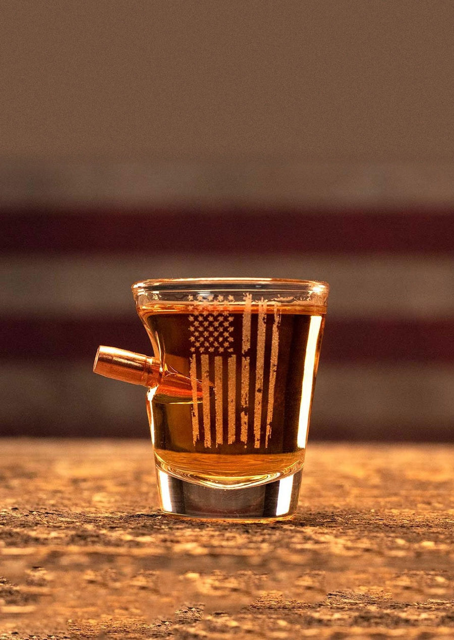 Shot glass with American flag design filled with a dark liquid on a wooden surface.