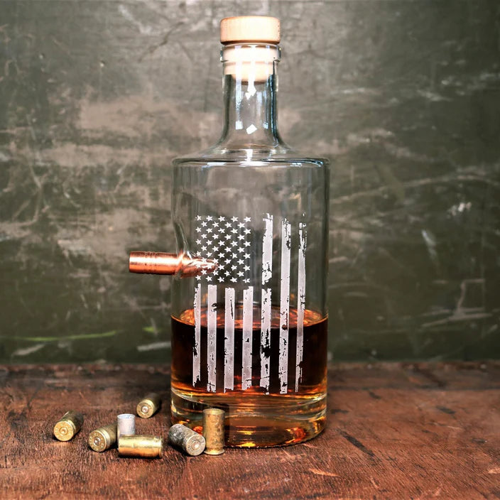 Glass whiskey decanter with American flag design and bullet on a wooden surface